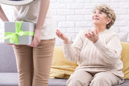 Happy senior woman sitting on a couch while being handed a gift box