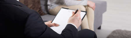 Close up of a psychoanalyst doing notes, in the background patient sitting on a sofa