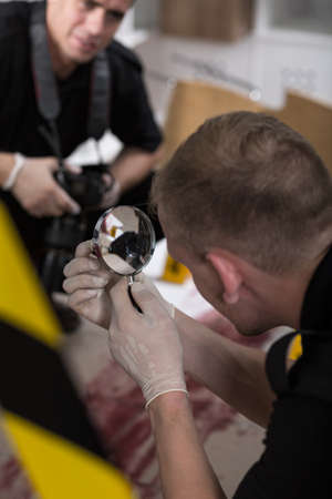 Policeman in white gloves holding a magnifier, police officer with a camera in the backgroundの写真素材