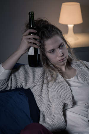 Shot of an upset young woman holding a bottle of wine next to her headの写真素材