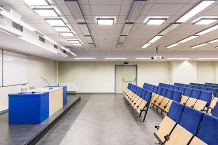 Lecture hall with desk and rows of seats, with navy blue elements