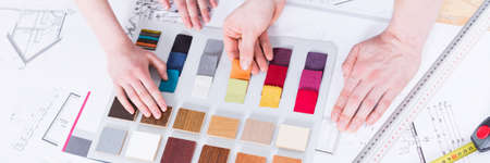 Paint samples lying on a table, close up of hands of two people, panoramaの写真素材