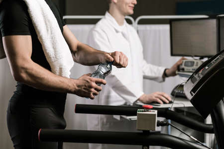 Sportsman is opening a bottle of water while the doctor is checking results on a screen
