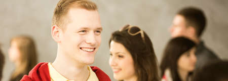 Young man smiling, standing in crowd of people, smiling woman in the background, panoramaの写真素材