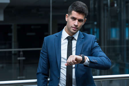 Shot of a young, smatrly-dressed man looking at his watch as if waiting for someoneの写真素材