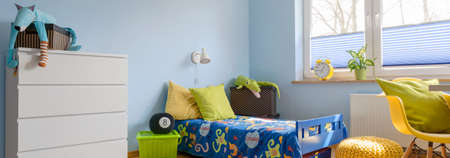 Colorful child room with small bed, decorative pillows, yellow chair and white chest of drawers