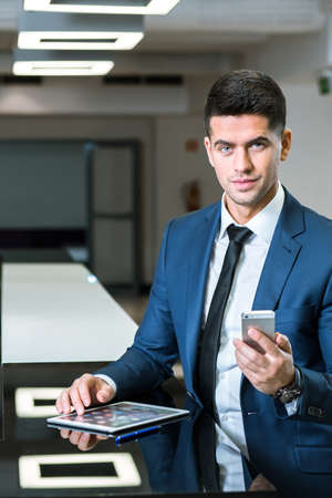 Close view of a young businessman at a worktop, using his tablet and mobile phone