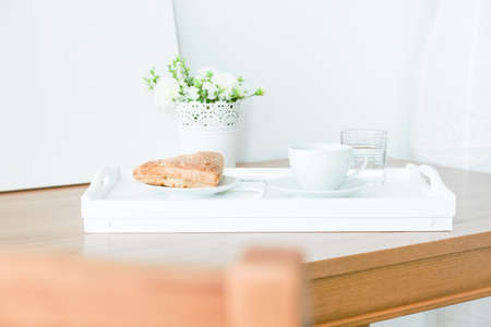 Close-up of plate with piece of pie and cup of coffee standing on a white tray. Prepared breakfast left on a wooden tableの写真素材