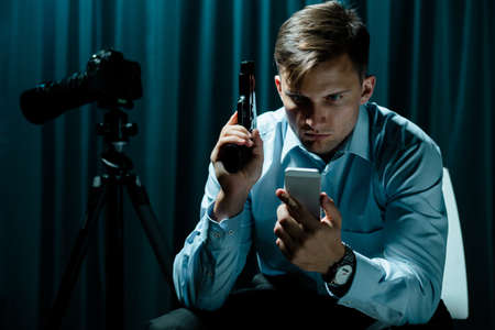 Man sitting in dar interior, using cellphone, holding gun