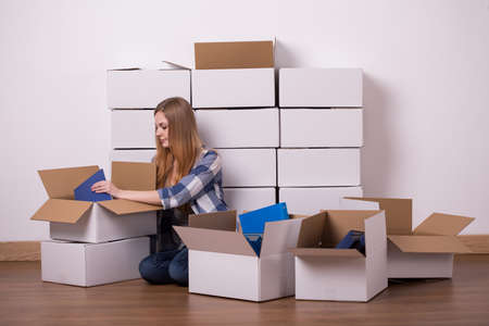 Shot of a young woman sitting on a floor and packing her things