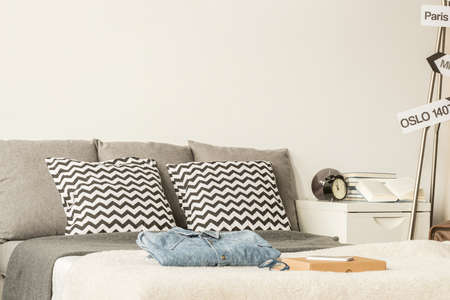 Large bed decorated with patterned pillows in a modern bedroom, with white nightstand and personal itemsの写真素材