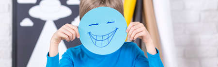 Shot of a little boy covering his face with a drawing of a smiling faceの写真素材