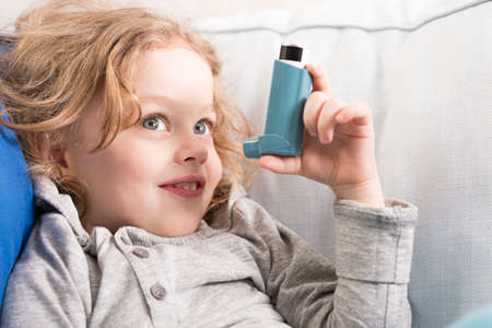 Small smiling boy holding inhaler, sitting on a light sofaの写真素材