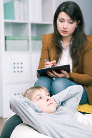 Shot of a young boy covering his ears and a psychologist trying to talk to himの写真素材