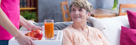 Panoramic picture of a smiling senior woman looking at a caregiver bringing her foodの写真素材