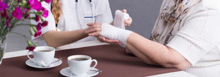 Close-up of young nurse taking care of older woman. Carer dressing a patient's wound. Next to them...