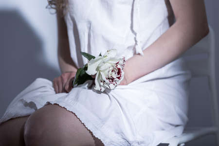 Close-up of a young woman's knees on which she is holding a white rose with red stainsの写真素材