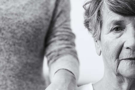 Old woman with sad eyes looking straight while somebody close to her is touching her shoulderの写真素材