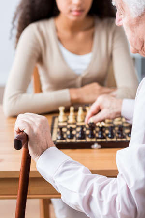 Senior man holding walking stick, playing chess with young womanの写真素材