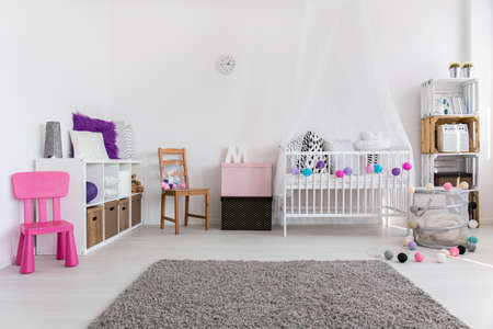 Spacious modern baby's room with soft grey carpet in the middle and white cradle by the wallの写真素材