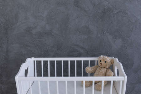 Shot of a teddy bear in a crib against a grey wallの写真素材