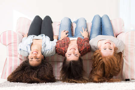 Shot of three happy young woman laying on a sofa with their heads down