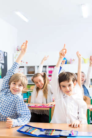 Smart little kids raising their hands to answer the question. Sitting in a classroom