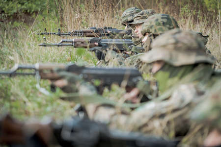 Hidden group of soldiers aiming rifles, lying on a groundの写真素材