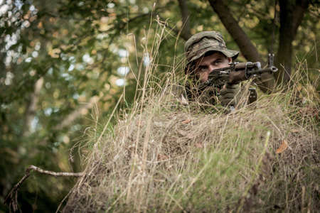 Young soldier pointing his gun from cover during training in forestの写真素材