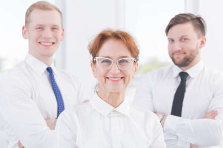 Image of happy mature businesswoman and two young businessmen standing in light interior