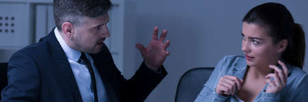 Frustrated female employee is sitting behind the desk and accept criticism from the bossの写真素材