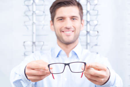 Happy man holding new pair of glasses, light backgroundの写真素材