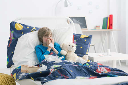 Shot of a young boy laying in a bed and blowing his noseの写真素材