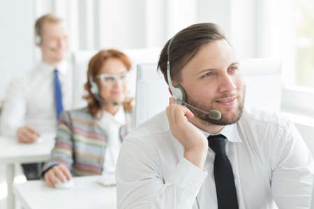 Handsome call center worker with headset sitting in light officeの写真素材