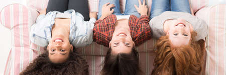Three happy friends smiling, sitting on sofa with heads upside down, panoramaの写真素材