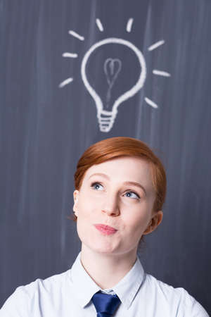 Young ginger businesswoman with a light bulb over her head, blackboard in the background