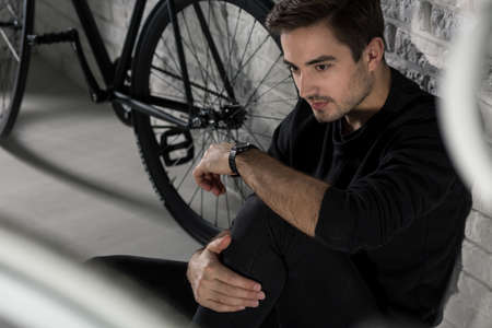 Shot of a young man wearing black clothes and sitting against a brick wall next to his bike