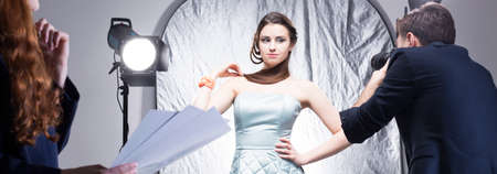 Beautiful photo model posing during session, stage manager with notes and photographer doing photos, panoramaの写真素材