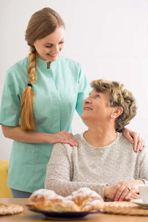 Portrait of an elderly woman and her home nurse standing behind her in an affectionate poseの写真素材