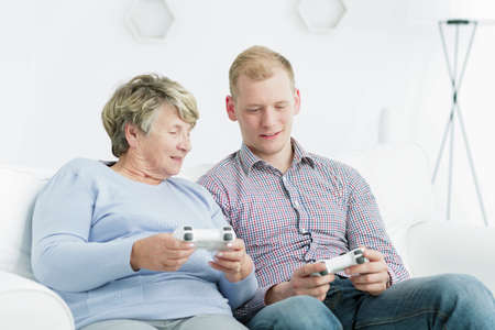 Elderly woman and young man sitting on a sofa, holding gamepads