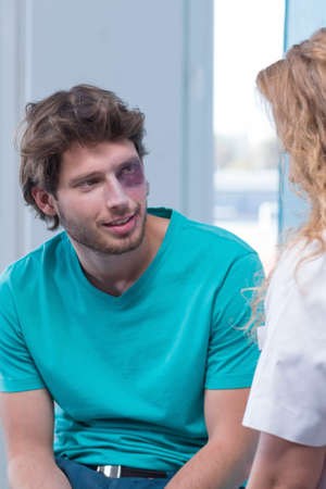 Shot of a young man with a black eye talking to a nurse in an emergency roomの写真素材