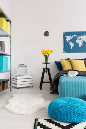 Cozy bedroom with large bed, decorative pillows and blue pouffe, light wallsの写真素材