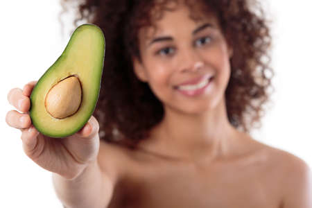Shot of a beautiful smiling young woman posing with a half of avocadoの写真素材