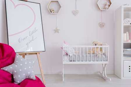 Fragment of a little girl's room with a white cradle and a picture frame on an easel with a cute printoutの写真素材