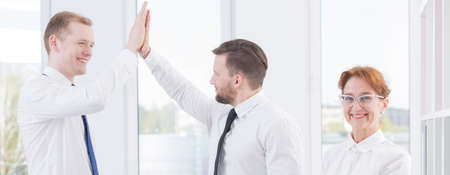 Shot of colleagues standing in an office and giving each other a high fiveの写真素材