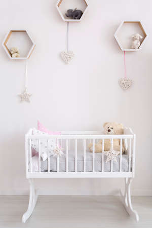 Close-up of a white cradle in a very bright baby room, with subtle decorations on the wallの写真素材