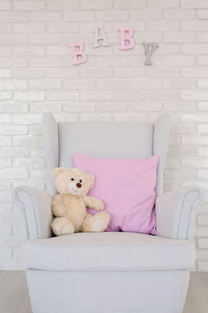 Close-up of an armchair with a cushion and a teddy bear by a white brick wall with decorative letters on itの写真素材