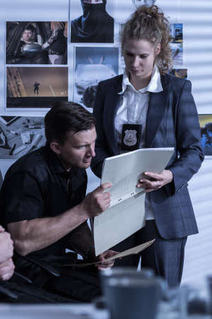 Woman with a badge and police officer analyzing filesの写真素材
