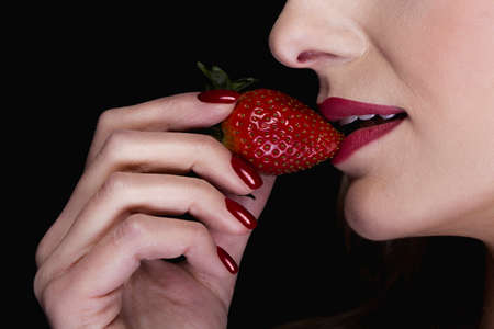 Close-up of a sexy woman holding a strawberry close to her red lipsの写真素材