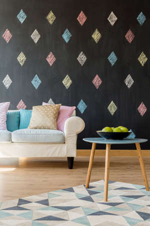 Image of a new flat with blackboard wall, pattern carpet, sofa, pastel cushions and small tableの写真素材